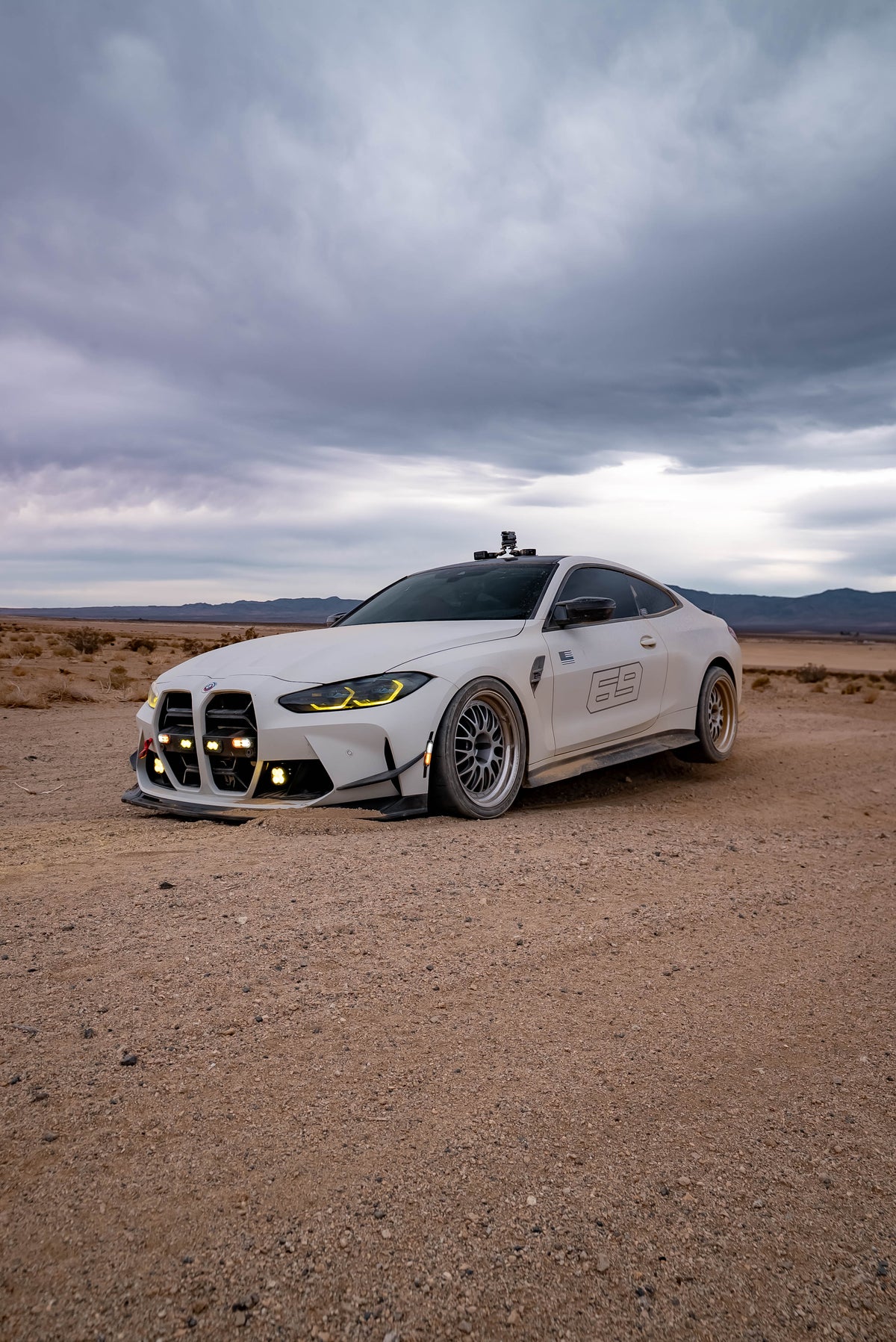 Front three-quarter view of a white coupe with auxiliary lights on a desert plain