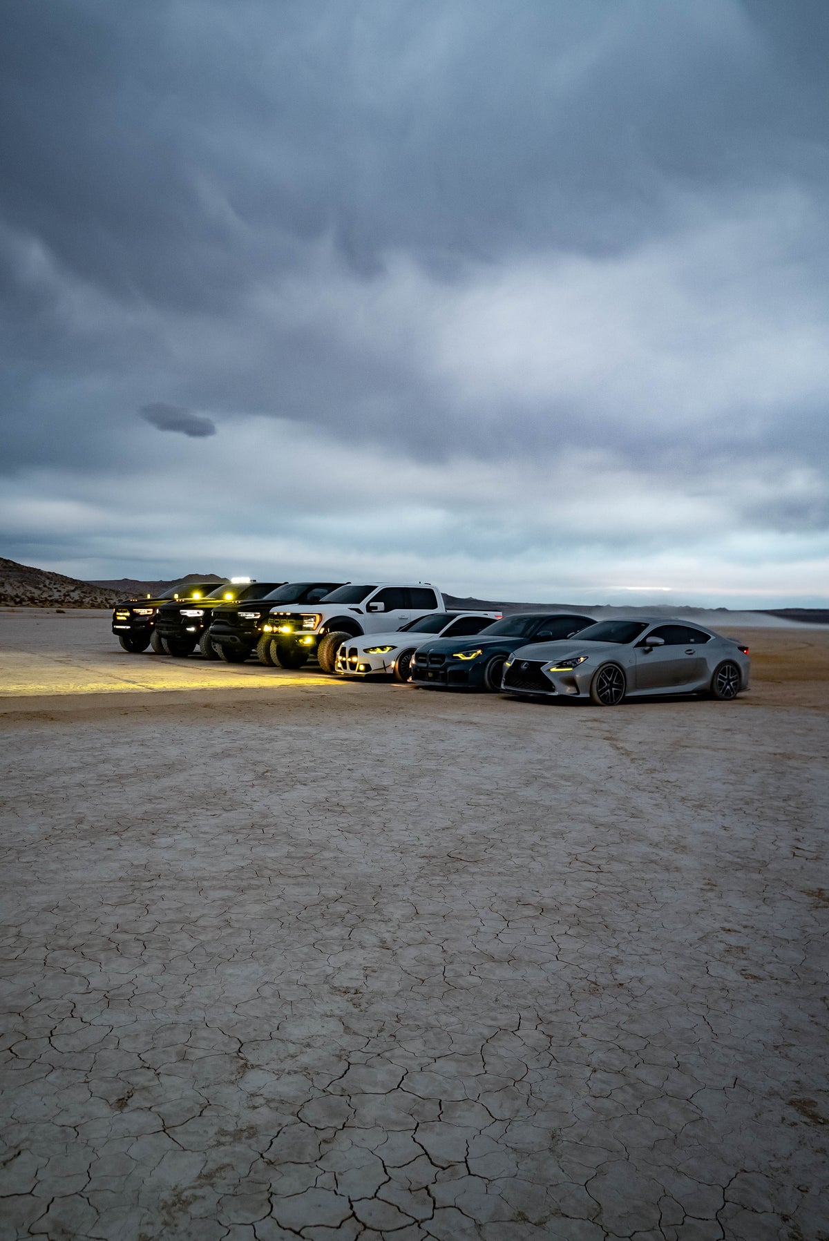 Cars and trucks parked together on a dry lakebed beneath a cloudy sky