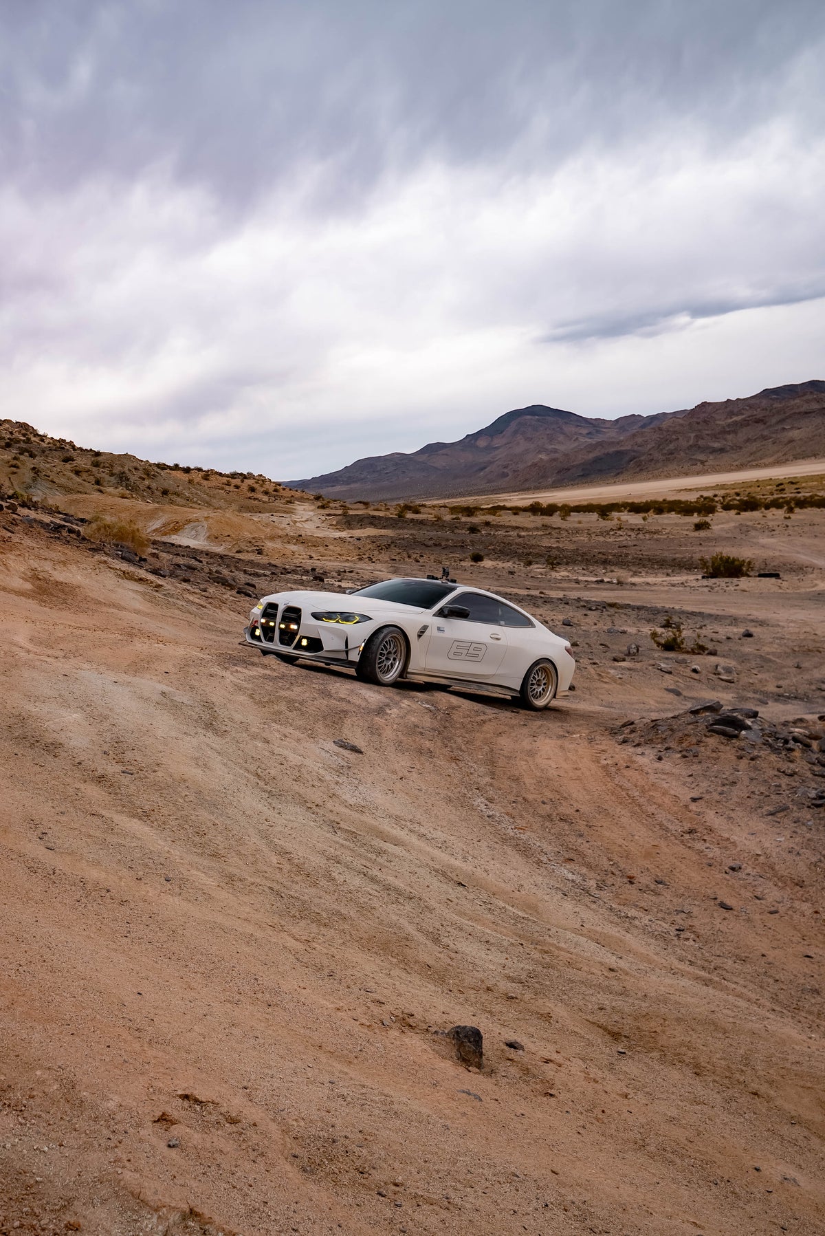 White coupe with front auxiliary lights on a rocky desert track
